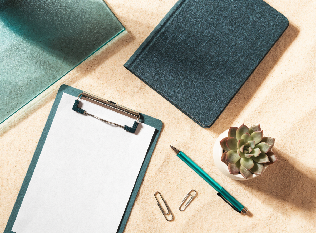 Clipboard, planner and pen on a sand-colored desk