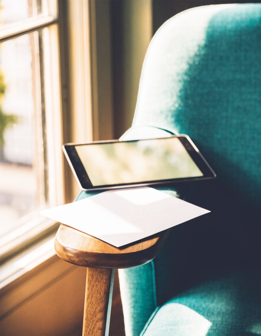 Tablet and printed page on a teal armchair by a window